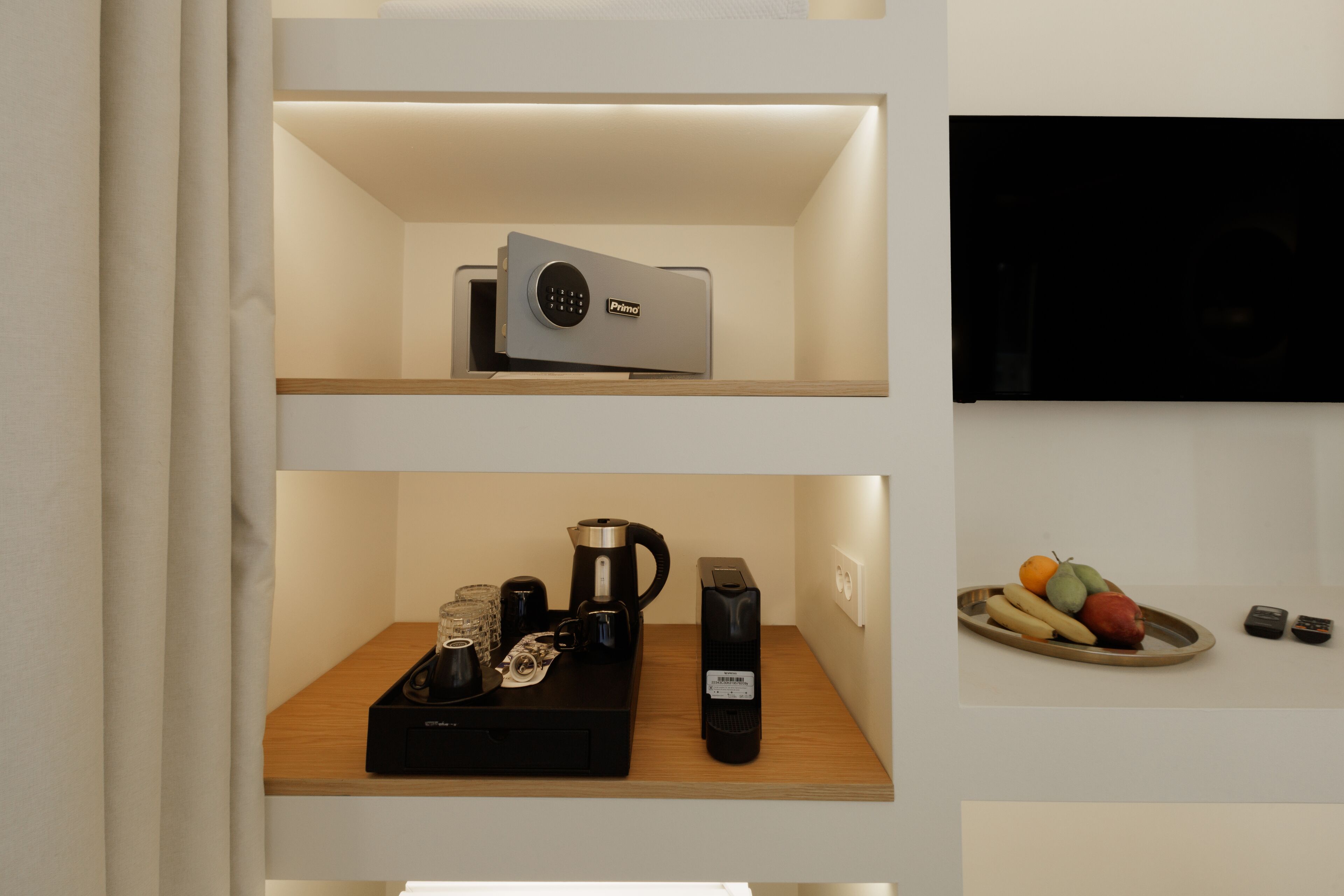 A shelf with a coffee maker, a remote control, and a tray of fruit.