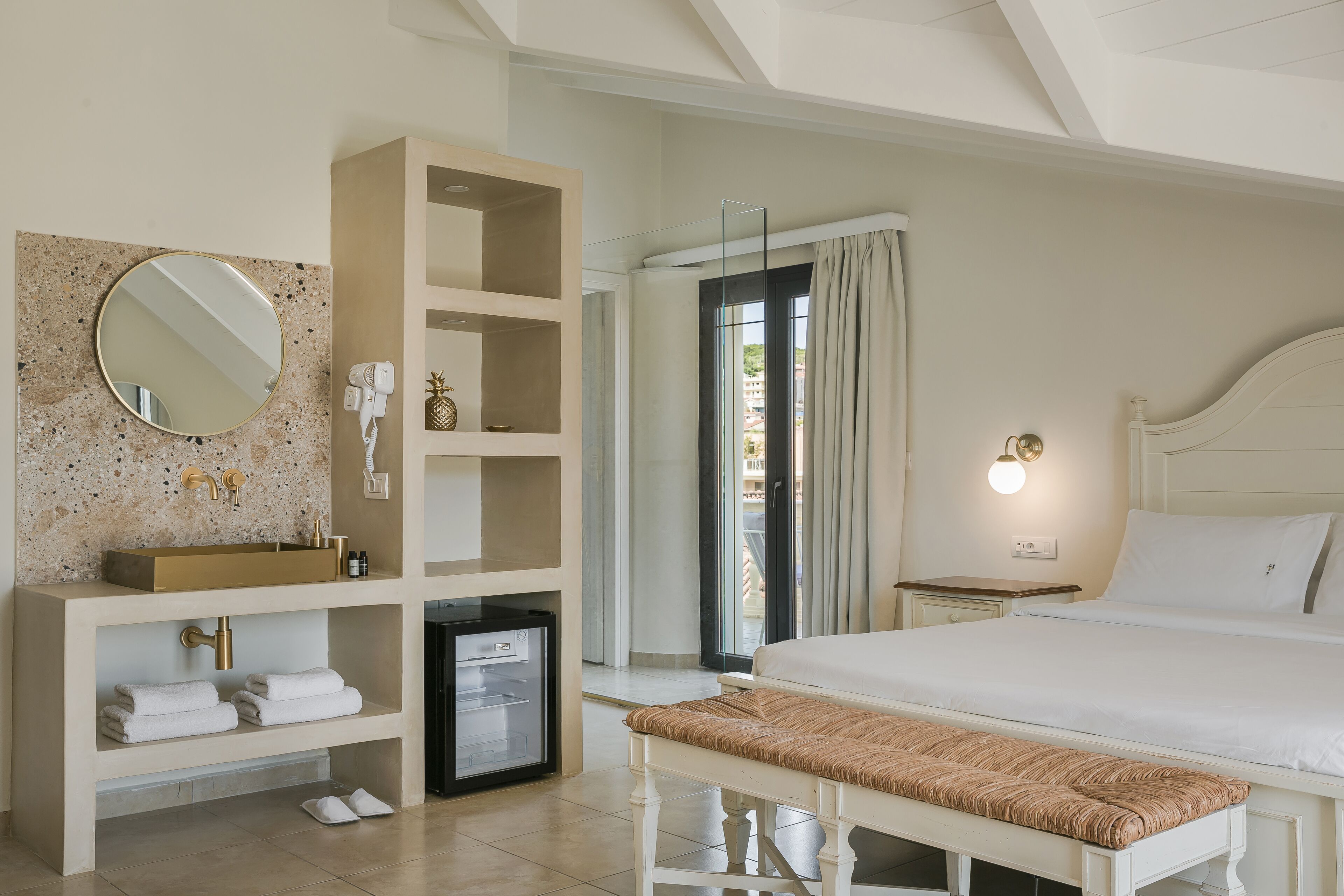 Ein Hotelzimmer mit einem Bett, einer Bank, einem Schminktisch mit Spiegel, einem kleinen Kühlschrank und einem Ablagefach mit Handtüchern.