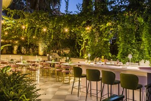 An outdoor dining area with tables and chairs, surrounded by lush greenery and string lights. - The Alley Hotel (Kefalonia)