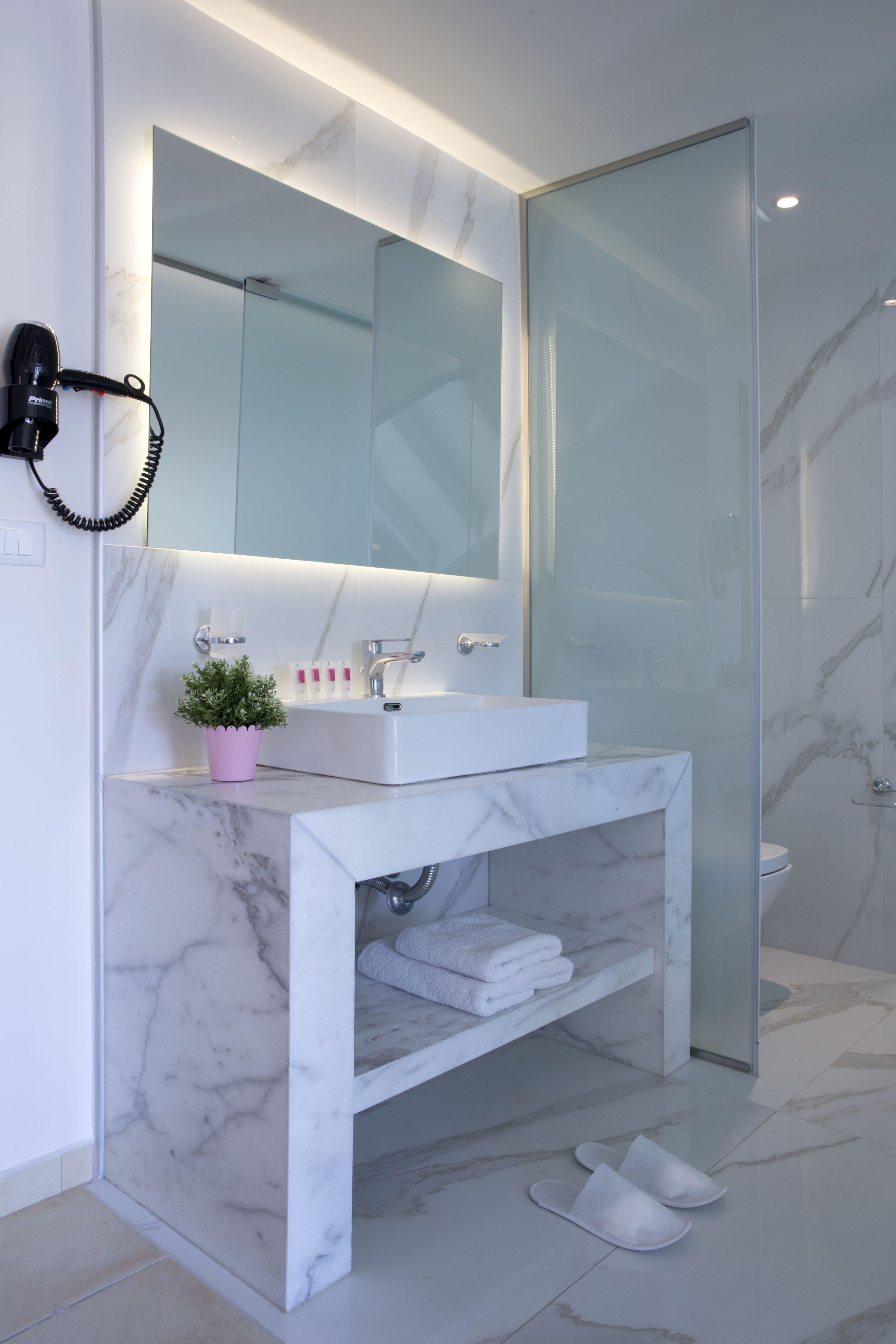 Un baño moderno con lavabo de mármol, cabina de ducha de vidrio y un secador de pelo montado en la pared.