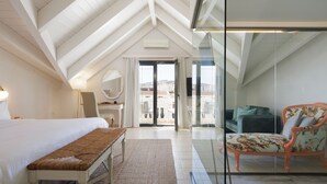Un dormitorio con una cama grande, un banco, una silla y un ventanal de vidrio que da a un espacio exterior.