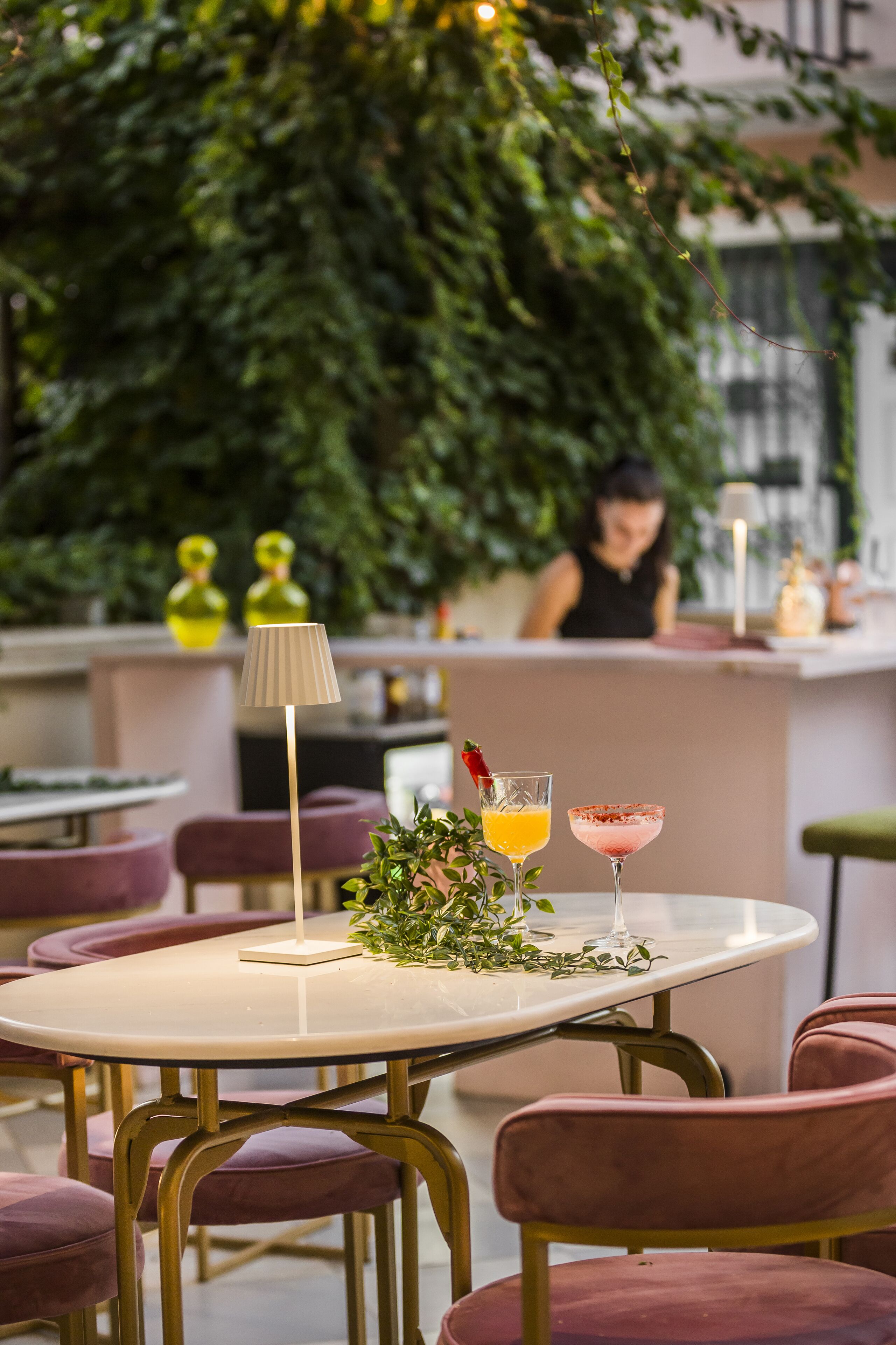 A restaurant interior with round tables, purple chairs, a bar area, and a green leafy backdrop.