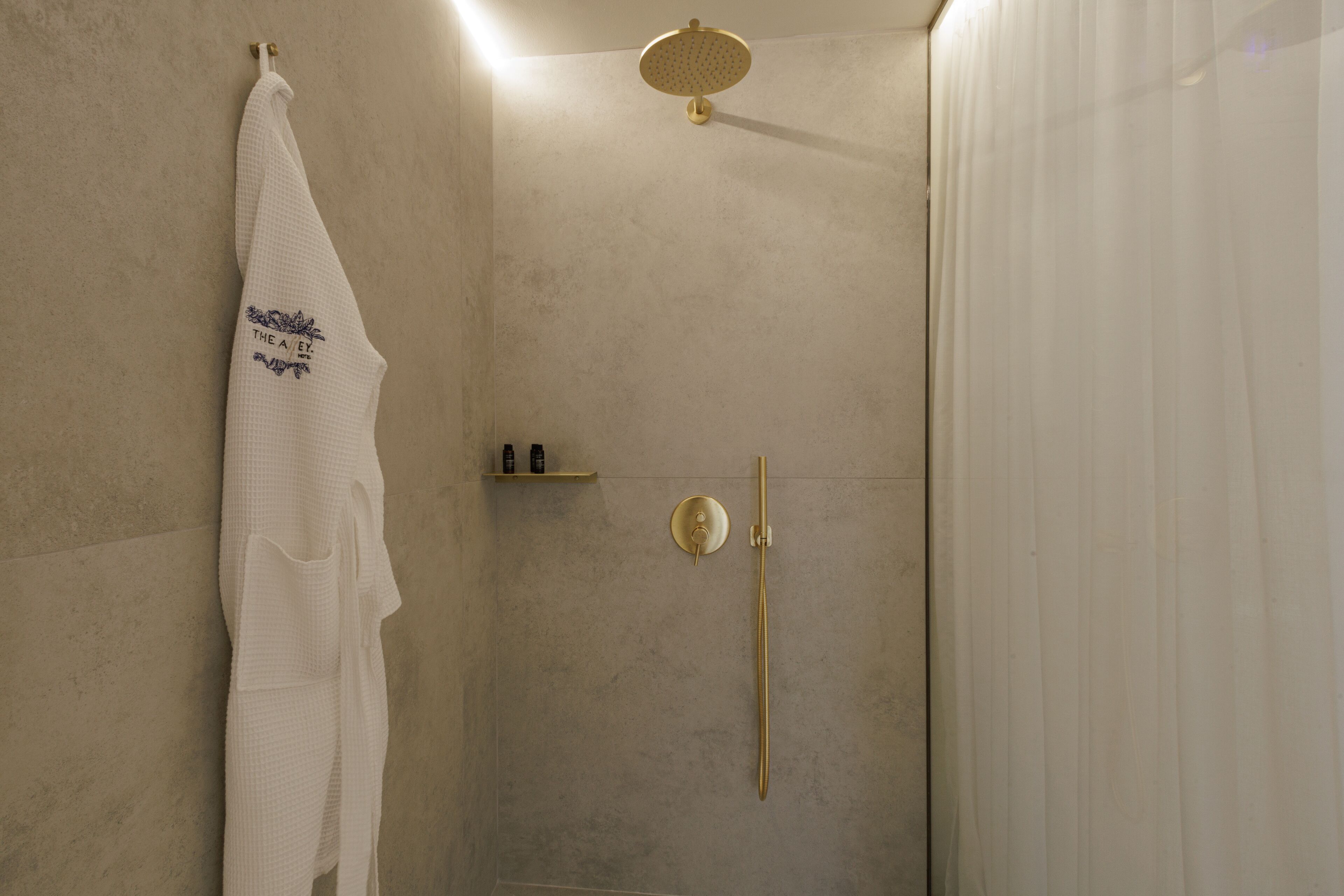 Un baño moderno con una pared color beige, una toalla blanca colgada en un gancho, un cabezal de ducha dorado y controles de ducha dorados.