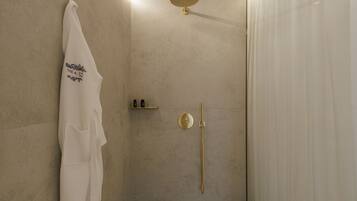 A modern bathroom with a beige wall, a white towel hanging on a hook, a gold showerhead, and a gold shower control.