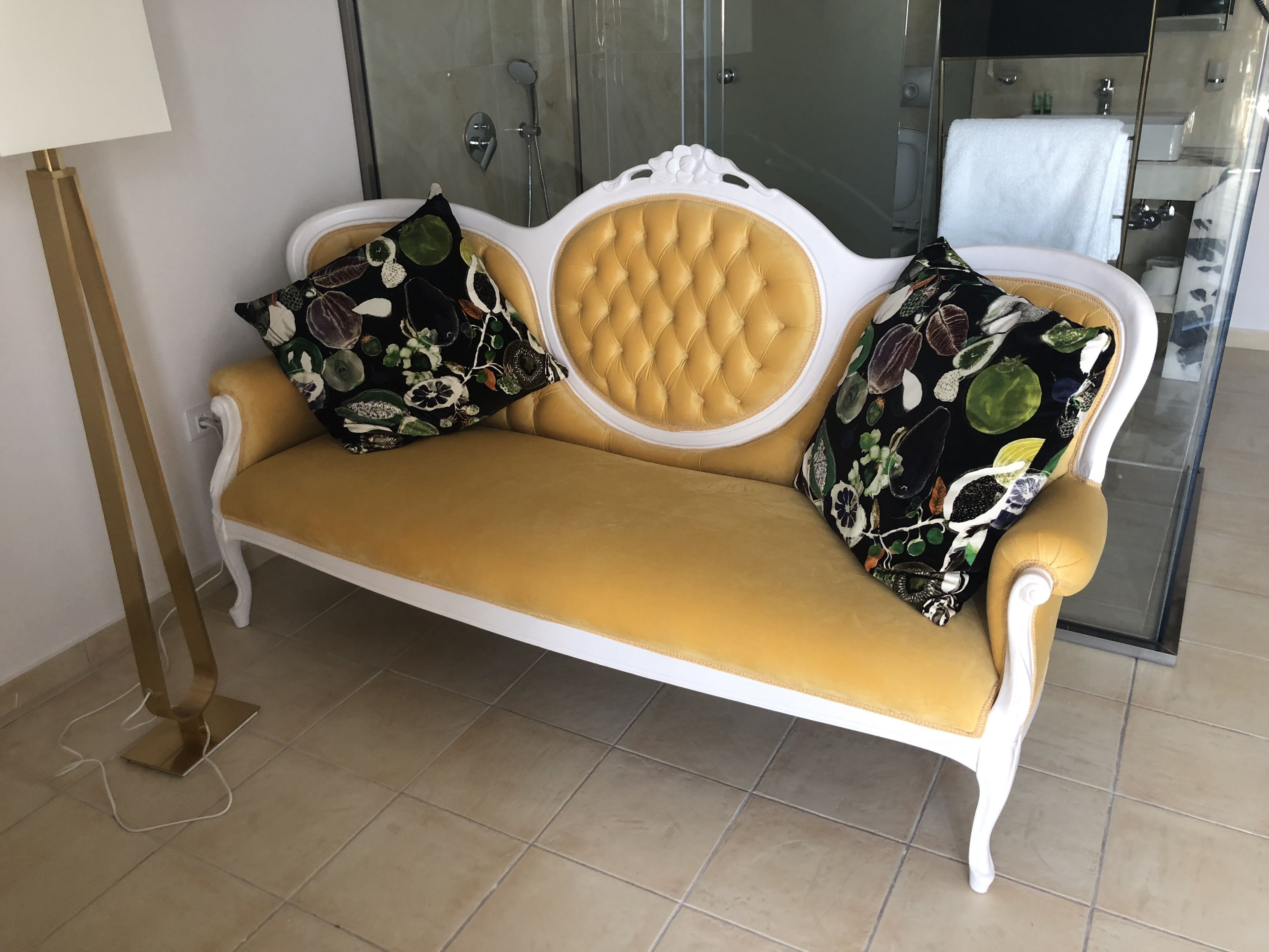 A sofa with floral cushions in a modern bathroom with a glass shower enclosure.
