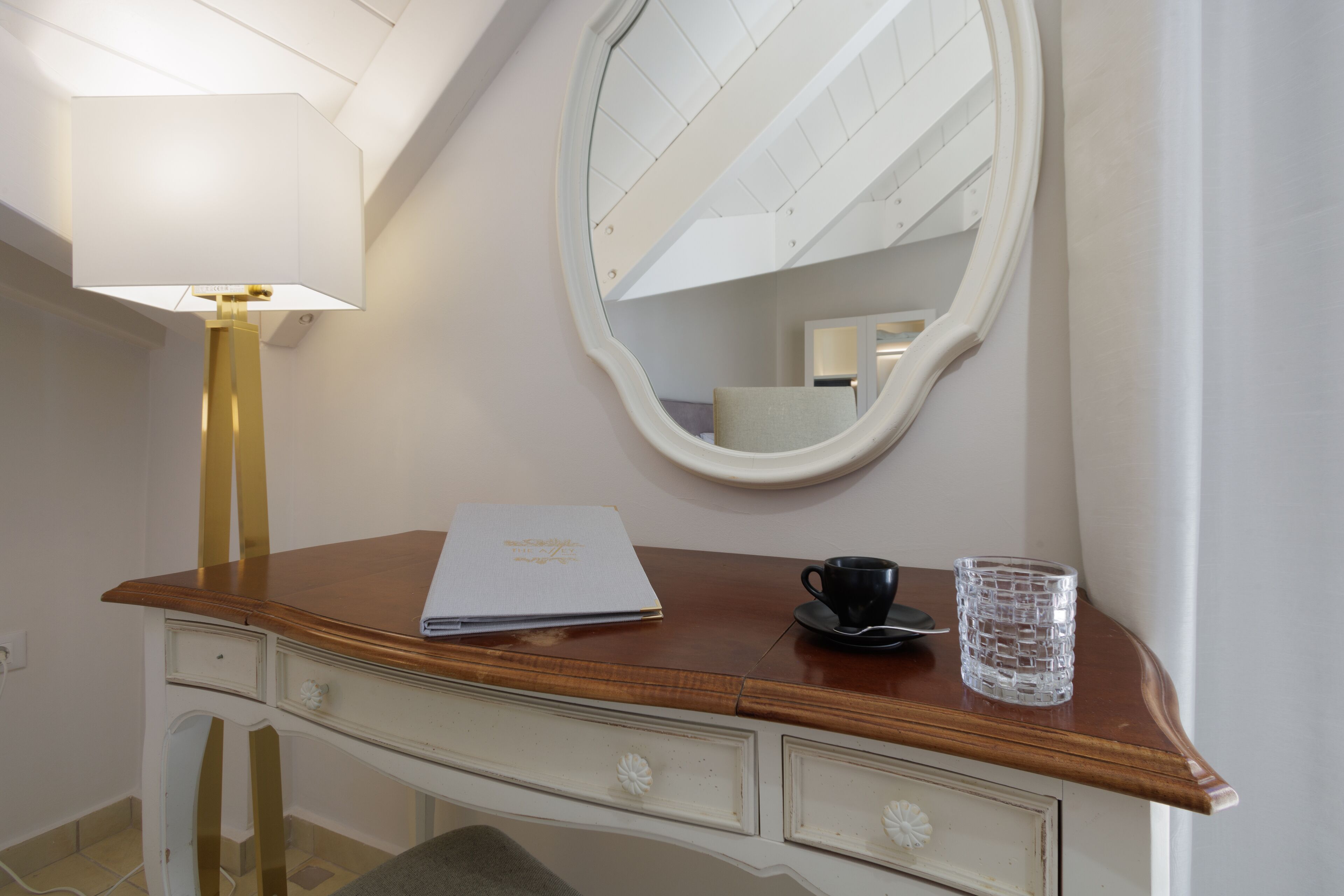 A wooden vanity with a mirror, a lamp, a cup, and a glass.