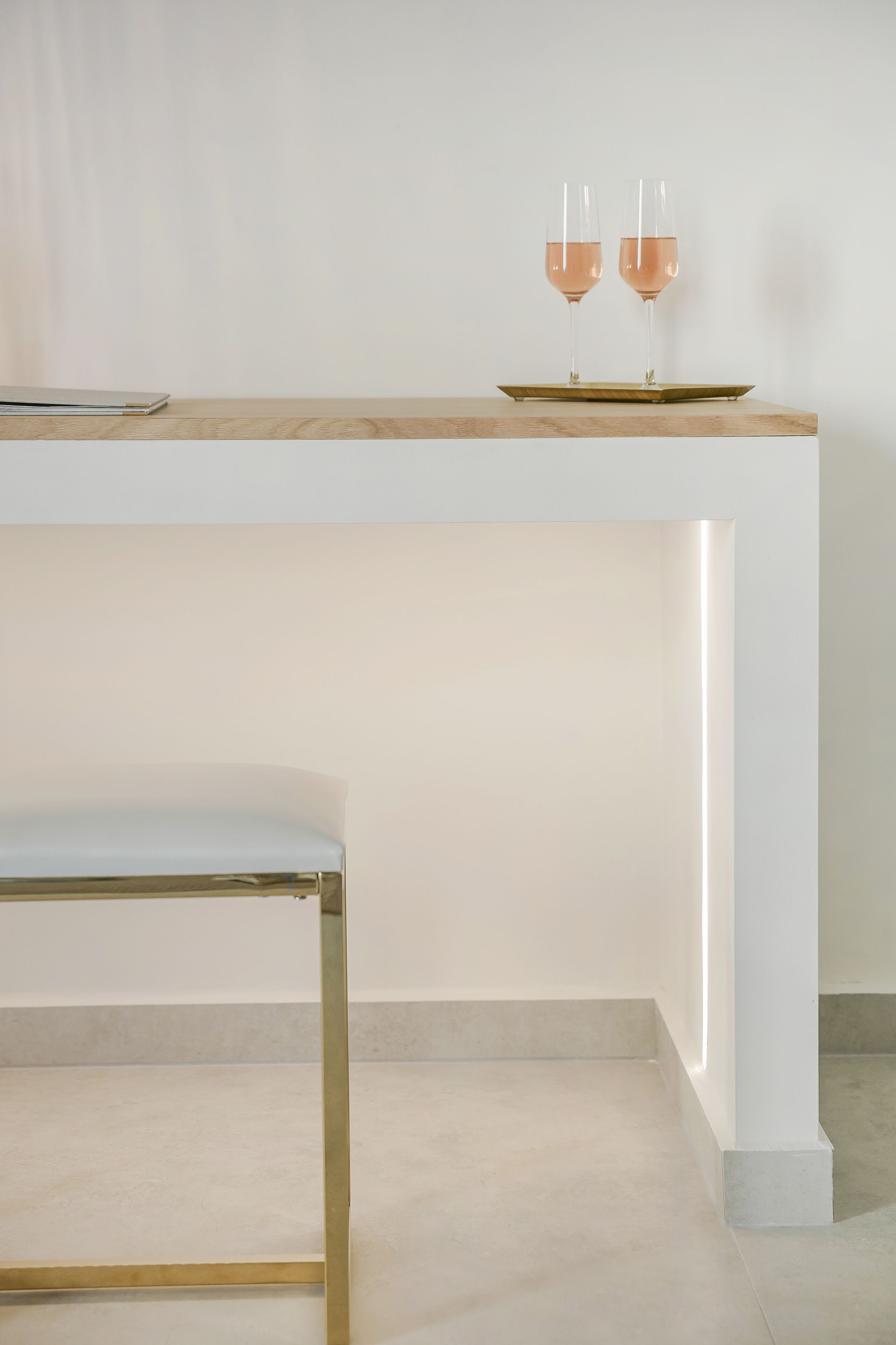 Een strakke bar met twee glazen rosé wijn op een dienblad, een barkruk en een schoon, modern design.