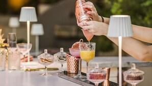 Un bar con una persona sirviendo una bebida en un vaso, rodeado de diferentes utensilios y copas de bar.