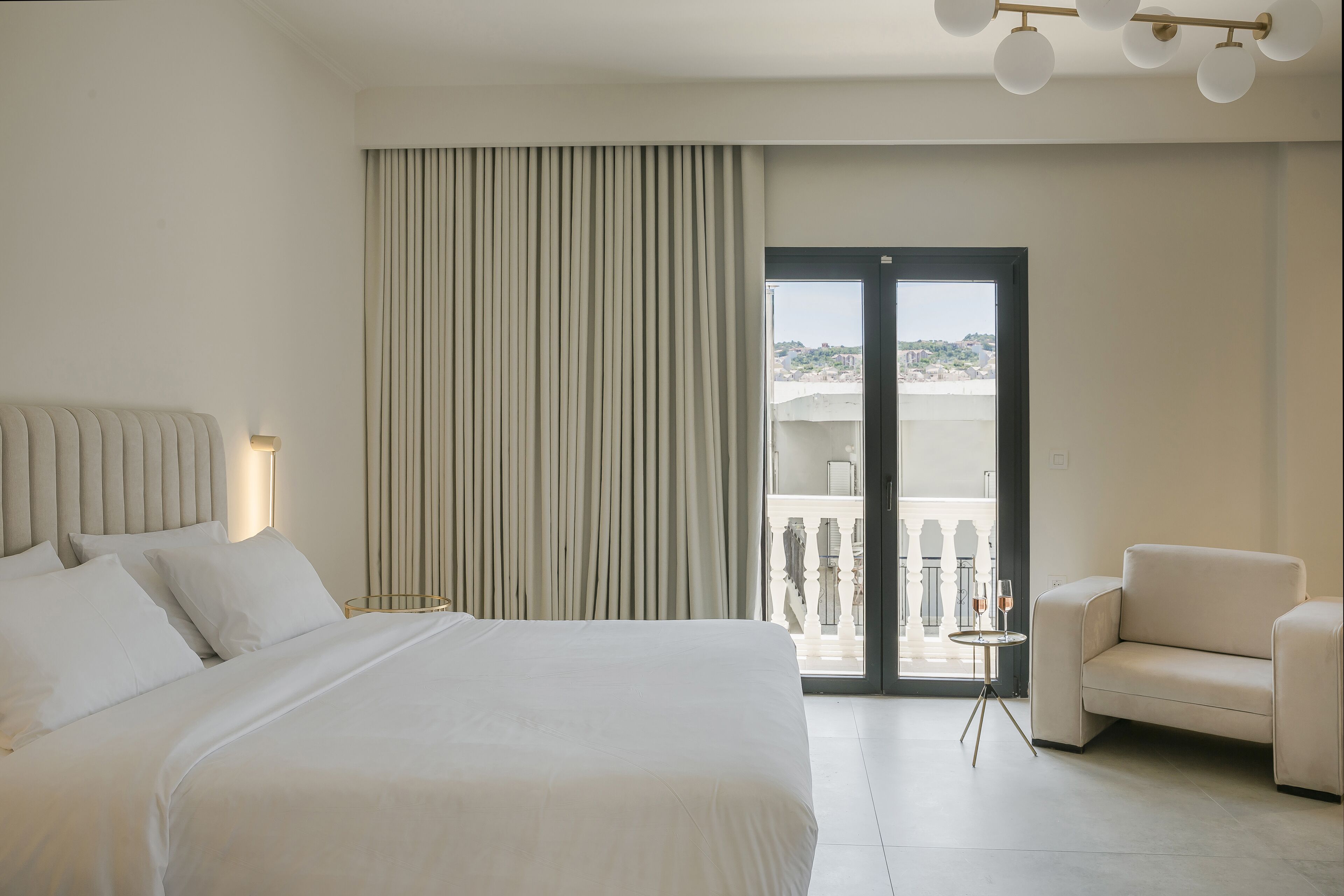 Une chambre d’hôtel avec un grand lit, un canapé, une petite table avec des verres et une vue sur la ville depuis la porte-fenêtre donnant sur le balcon.