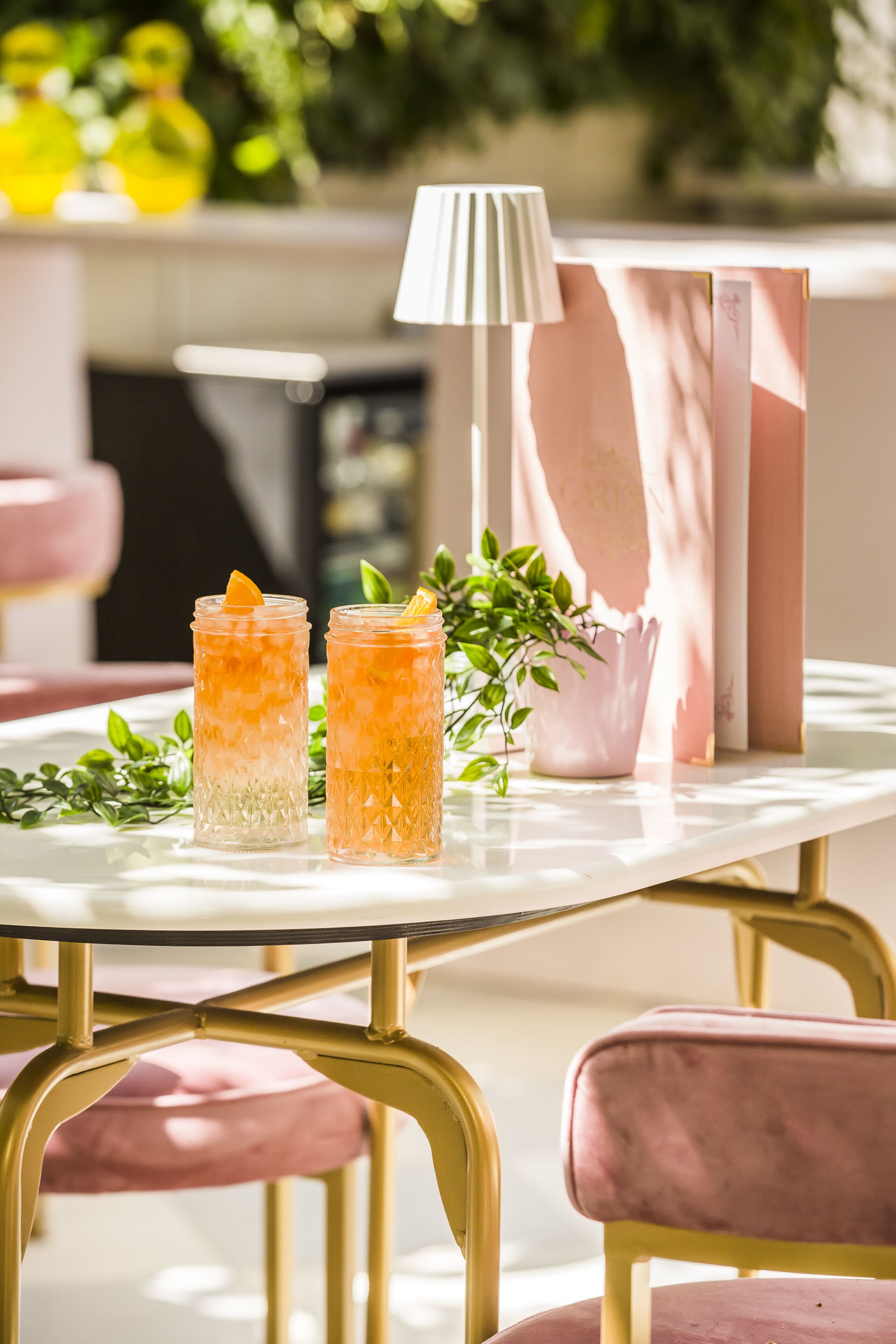 A table with two glasses of orange beverage, a potted plant, and a pink vase.