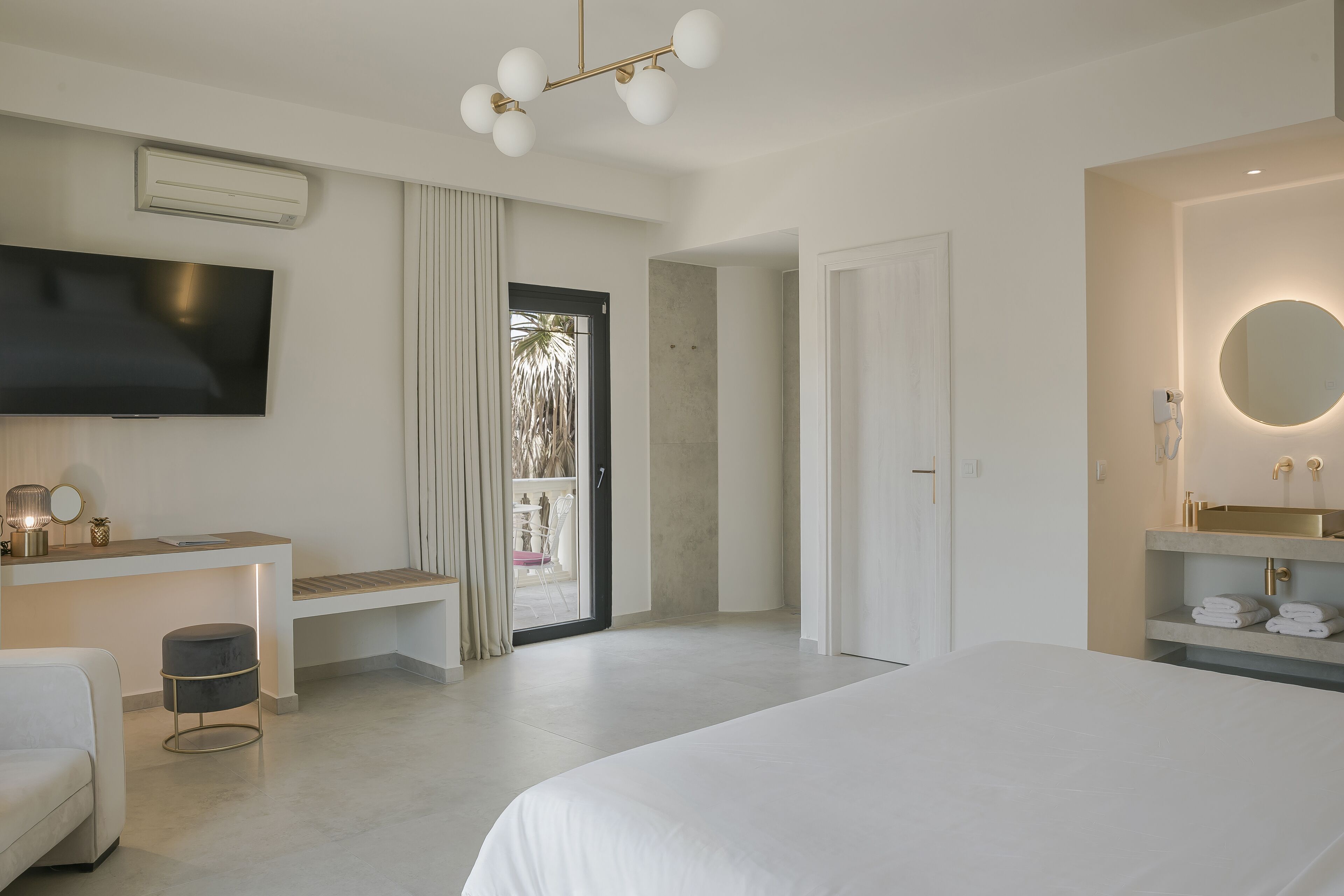 Una habitación de hotel moderna con una cama grande, un televisor de pantalla plana, un escritorio con una silla y un baño con un espejo redondo.