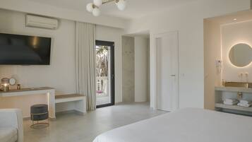 Una habitación de hotel moderna con una cama grande, un televisor de pantalla plana, un escritorio con una silla y un baño con un espejo redondo.