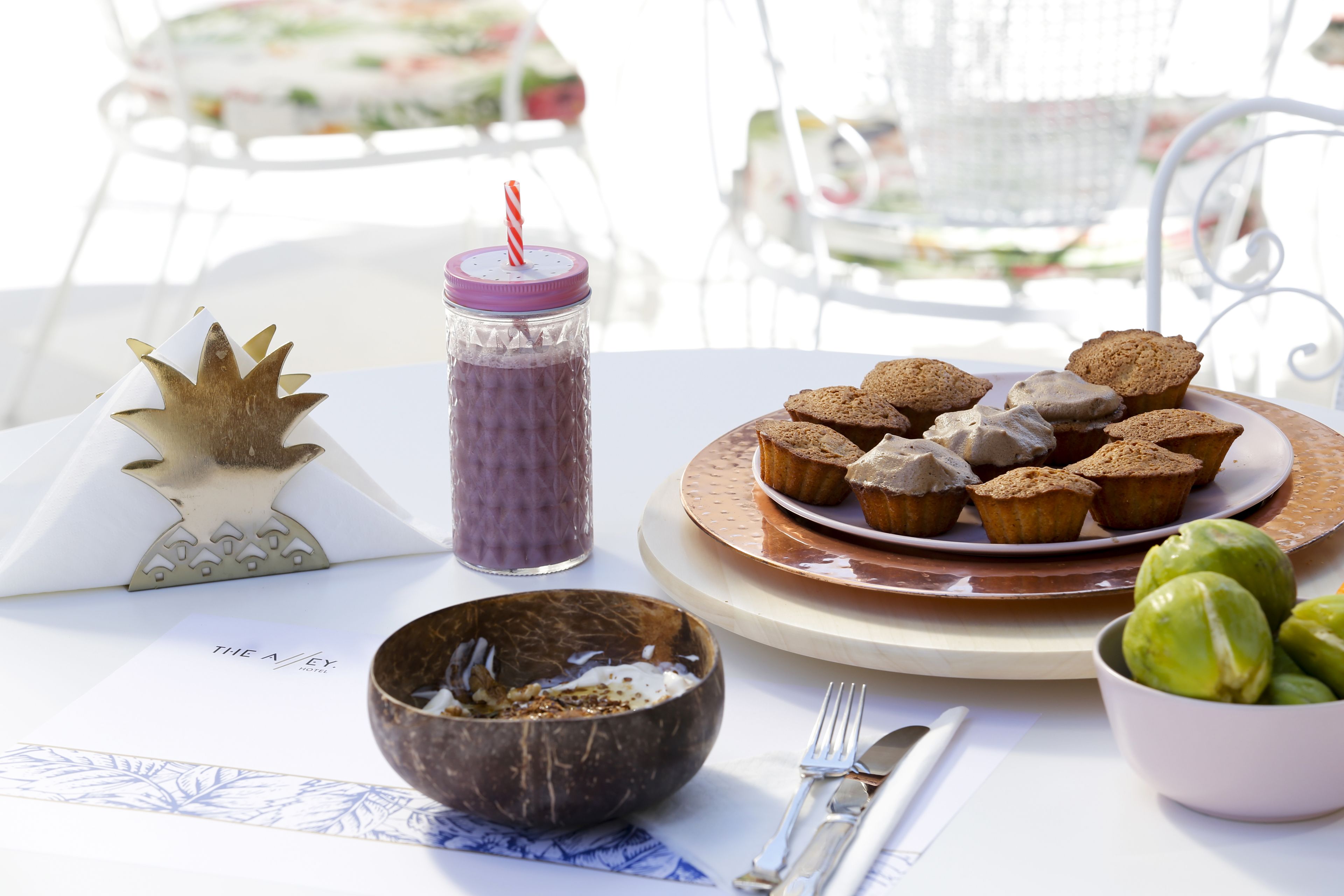 A table with a plate of muffins, a jar with a straw, a decorative item, a bowl, and a menu.