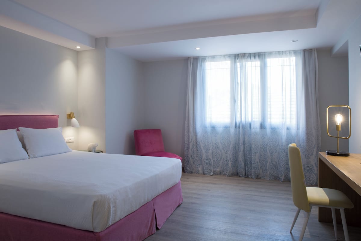 A modern hotel room with a large bed, a desk, and a chair.