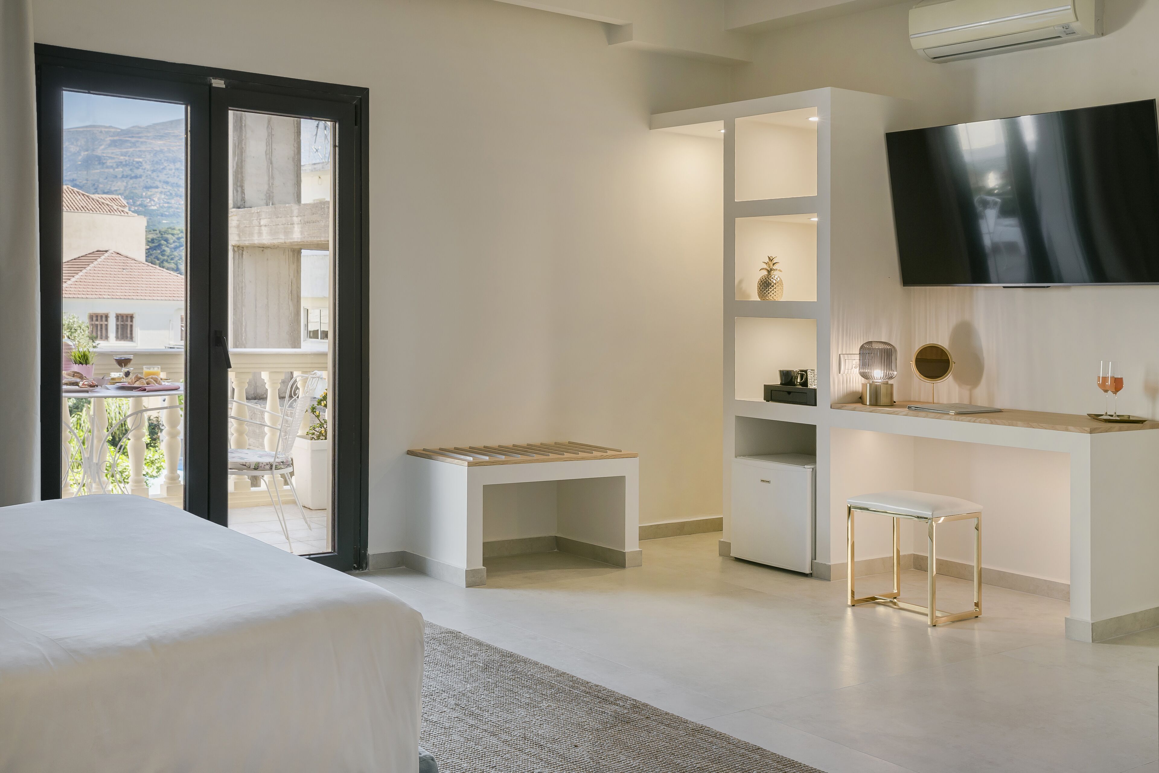 A modern hotel room with a balcony, a bed, a desk, and a TV.