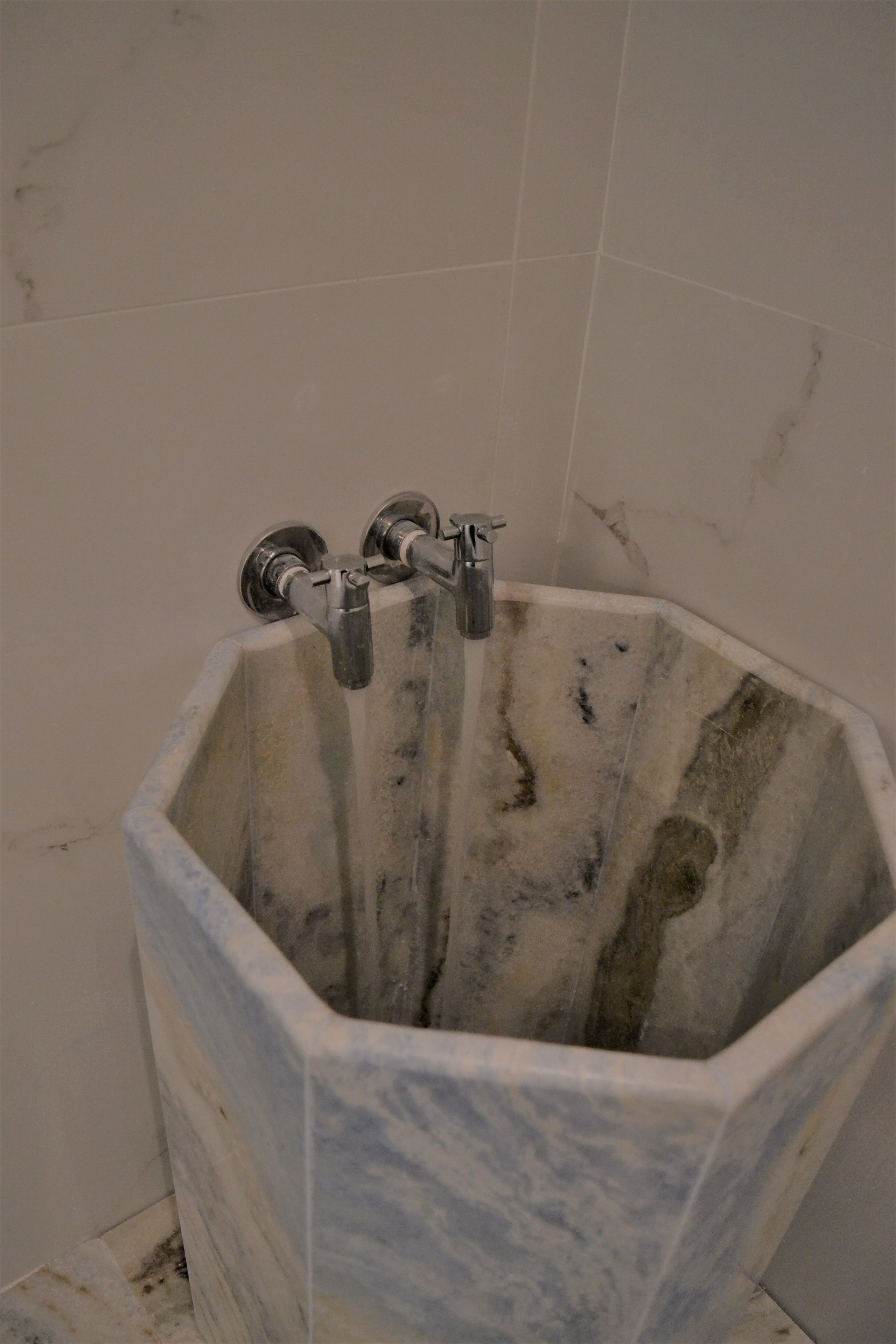 A bathroom with a large, octagonal marble sink and two faucets.