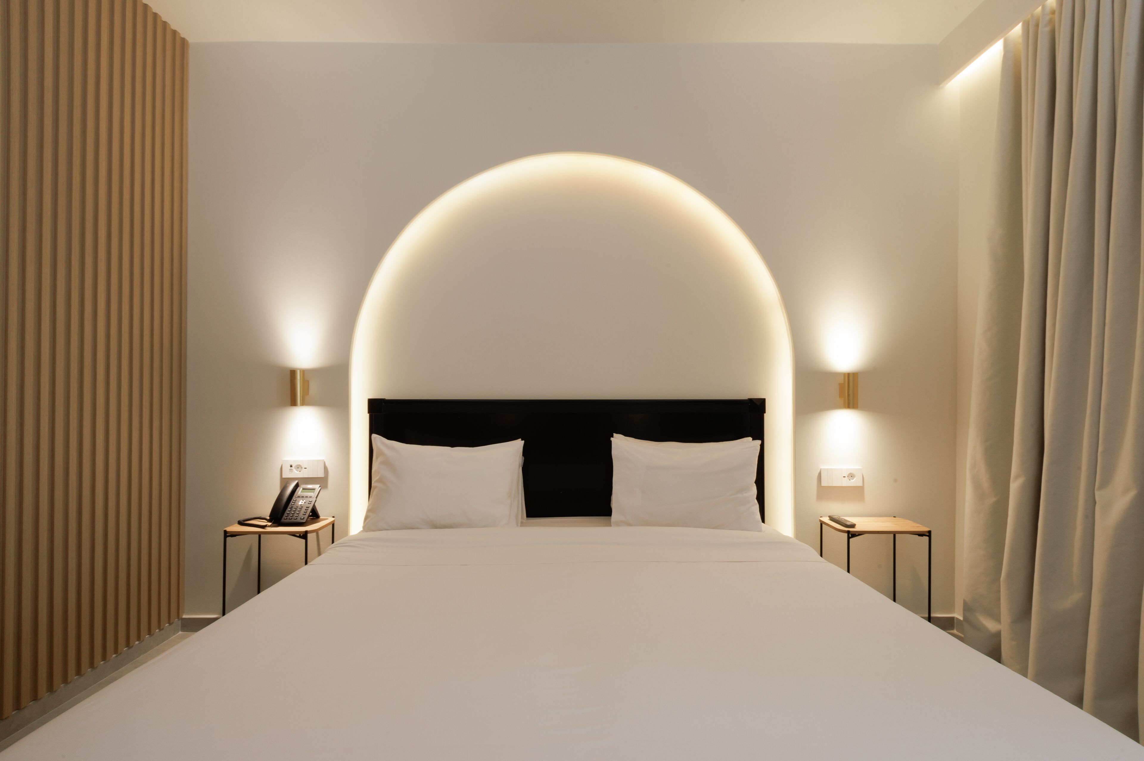 A hotel room with a large bed, two bedside tables with lamps, a phone on one table, and a curtain on the window.