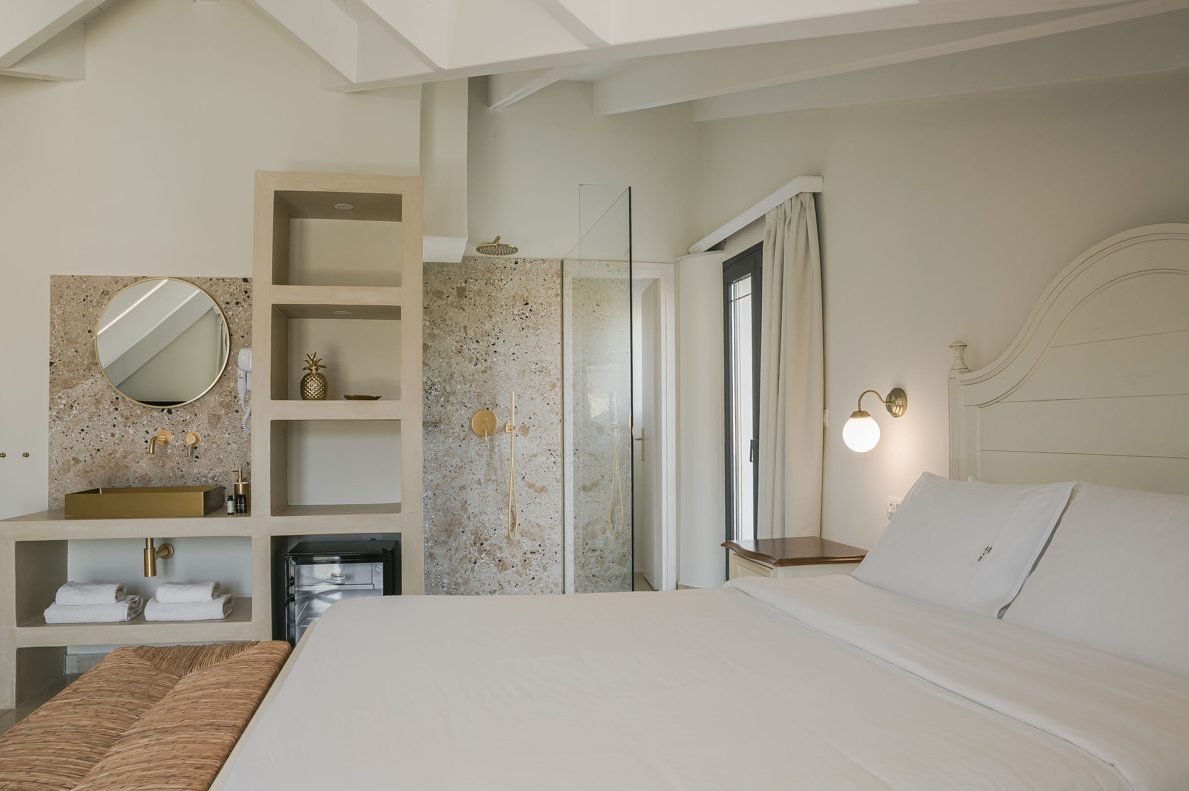 A modern hotel room with a large bed, a built-in vanity with a mirror, a shower, and a bedside table with a lamp.