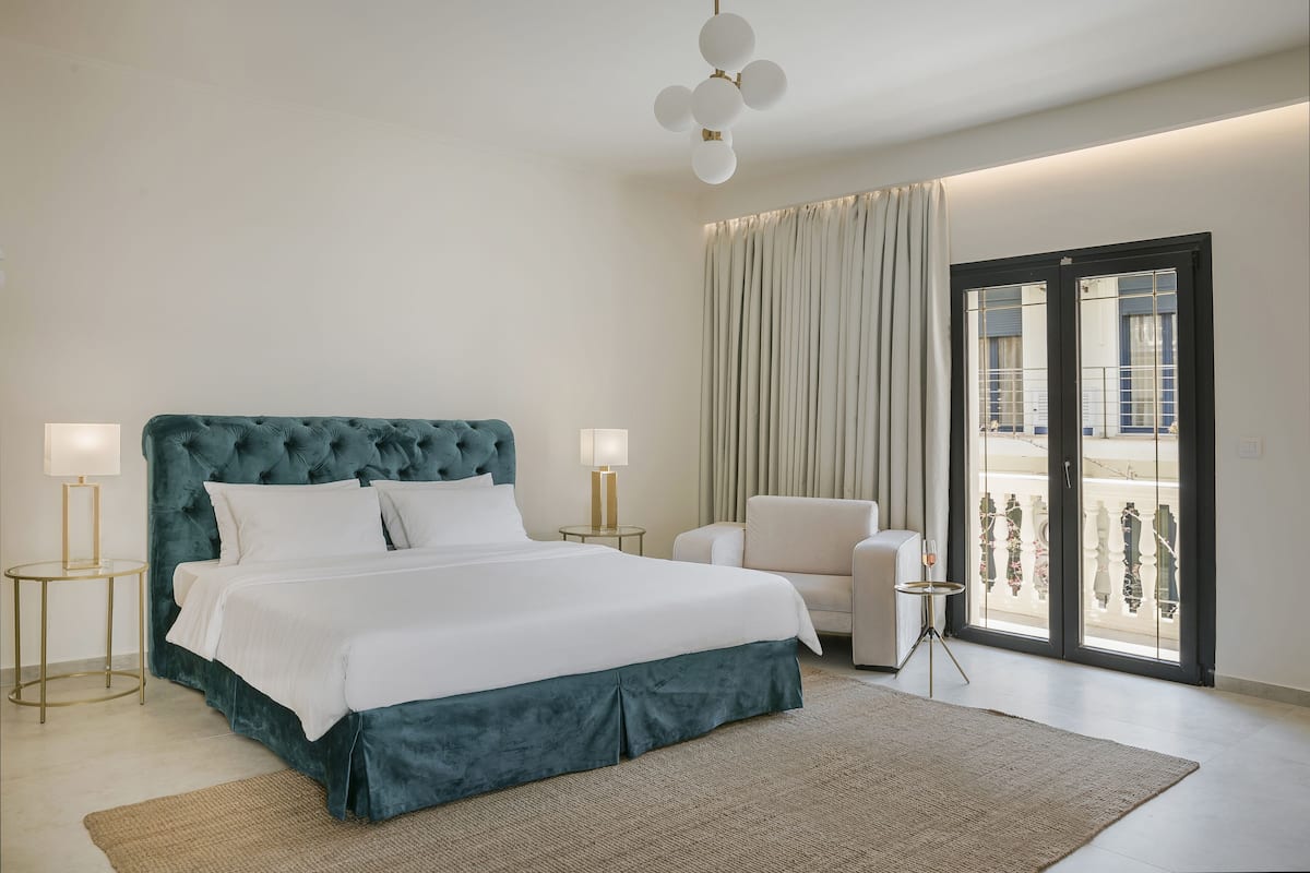 A modern hotel room with a large bed, two bedside tables, a chair, and a balcony with curtains.