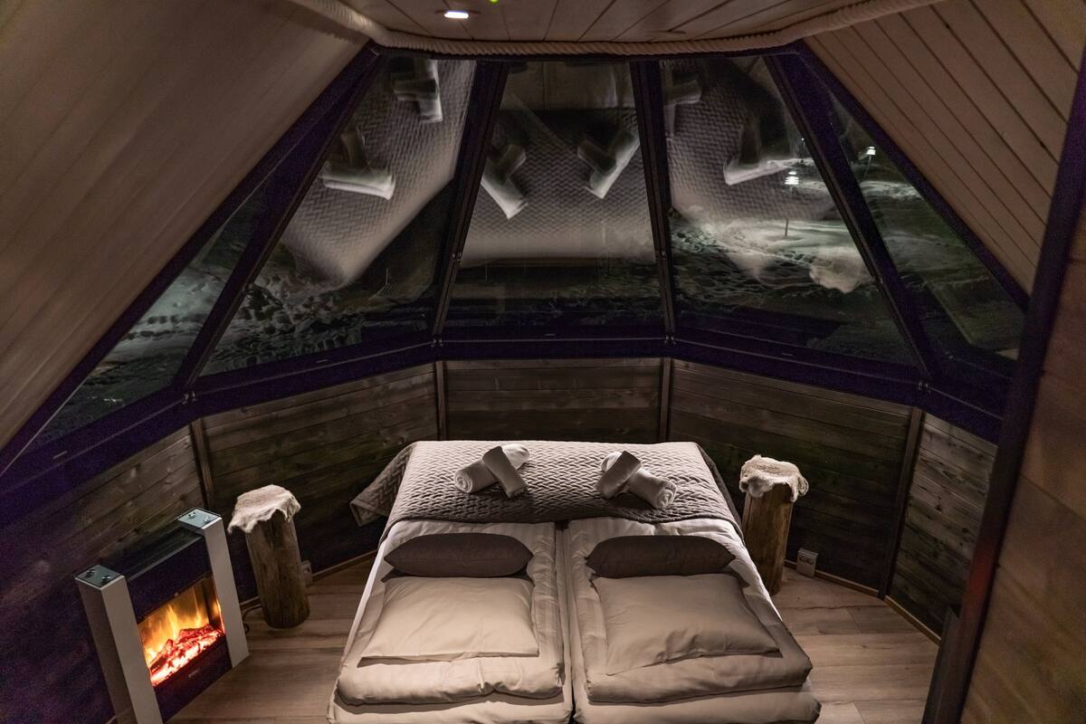 Una habitación acogedora con una cama, una chimenea y vistas al exterior a través de un amplio ventanal.