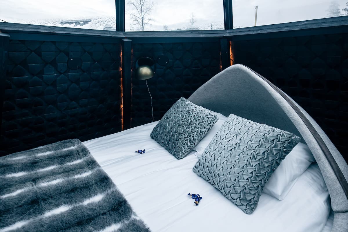 Un dormitorio moderno con un ventanal grande, una cama con almohadas estampadas y una manta de piel.