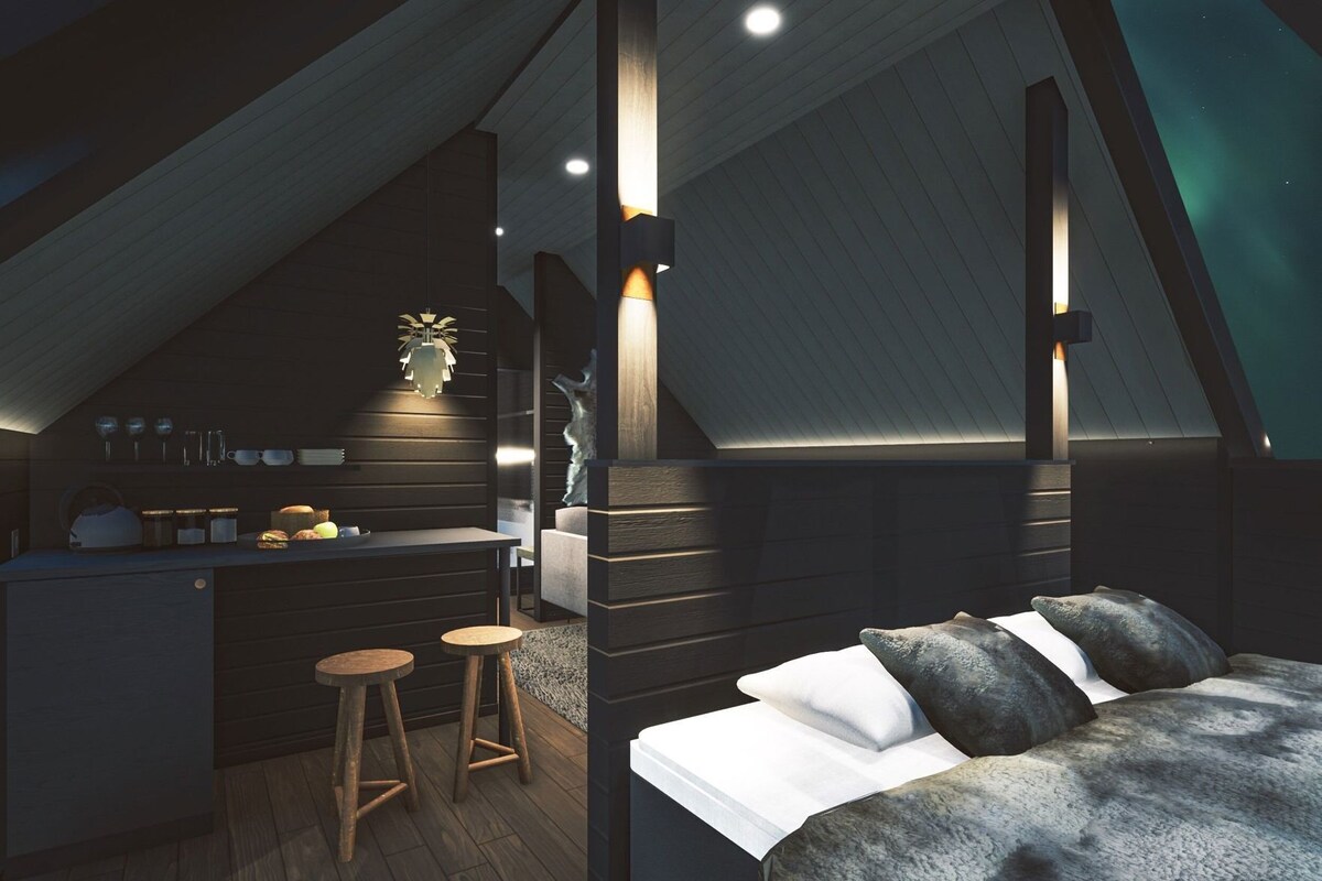 A modern loft bedroom with a sloped ceiling, a built-in kitchen area, and a cozy seating space.