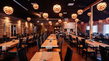 A restaurant with wooden tables and chairs, hanging pendant lights, and a Christmas tree.