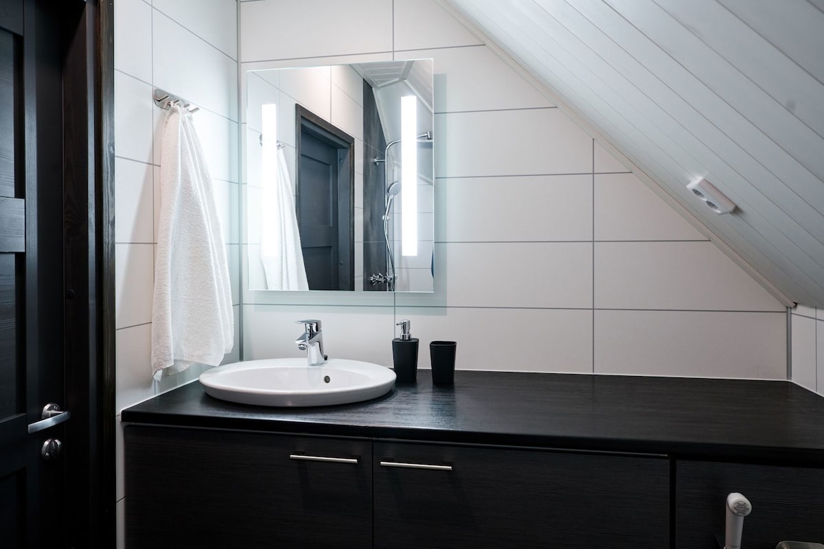 A modern bathroom with a white sink, dark cabinetry, and a large mirror.