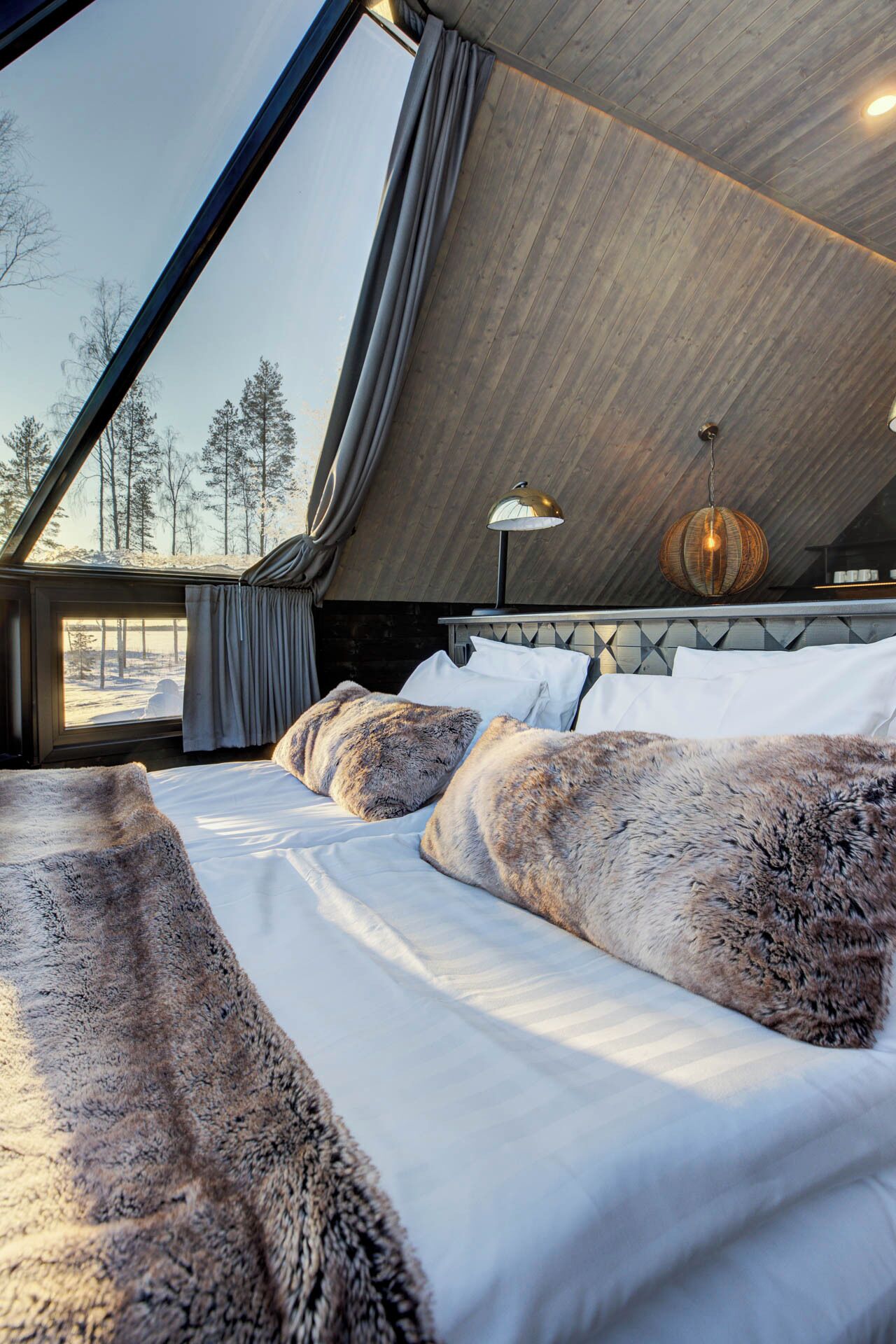 Een knus slaapkamer met een groot bed, een bontje en uitzicht op een besneeerd landschap door een raam.