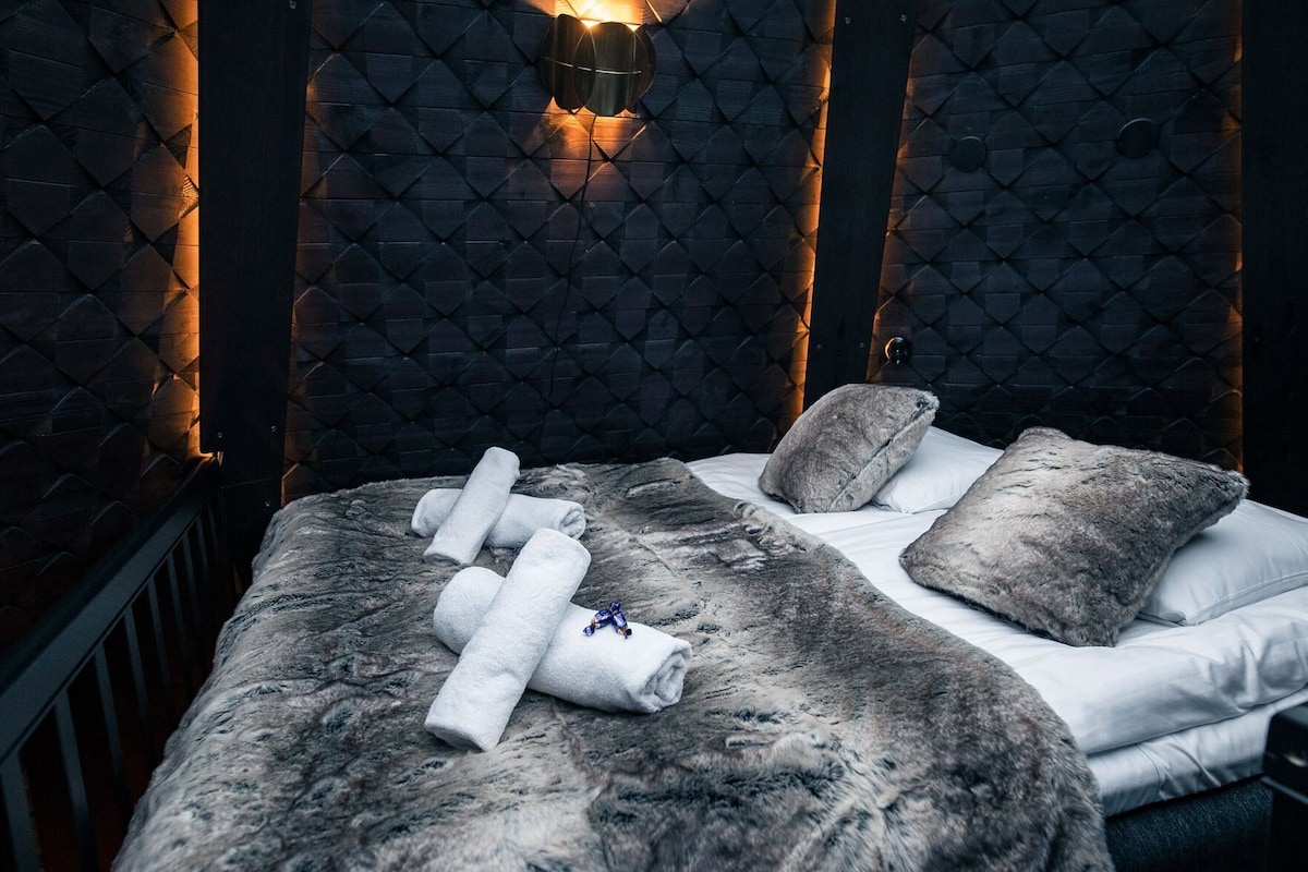 A bed with a fur-like cover, two pillows, and rolled towels.