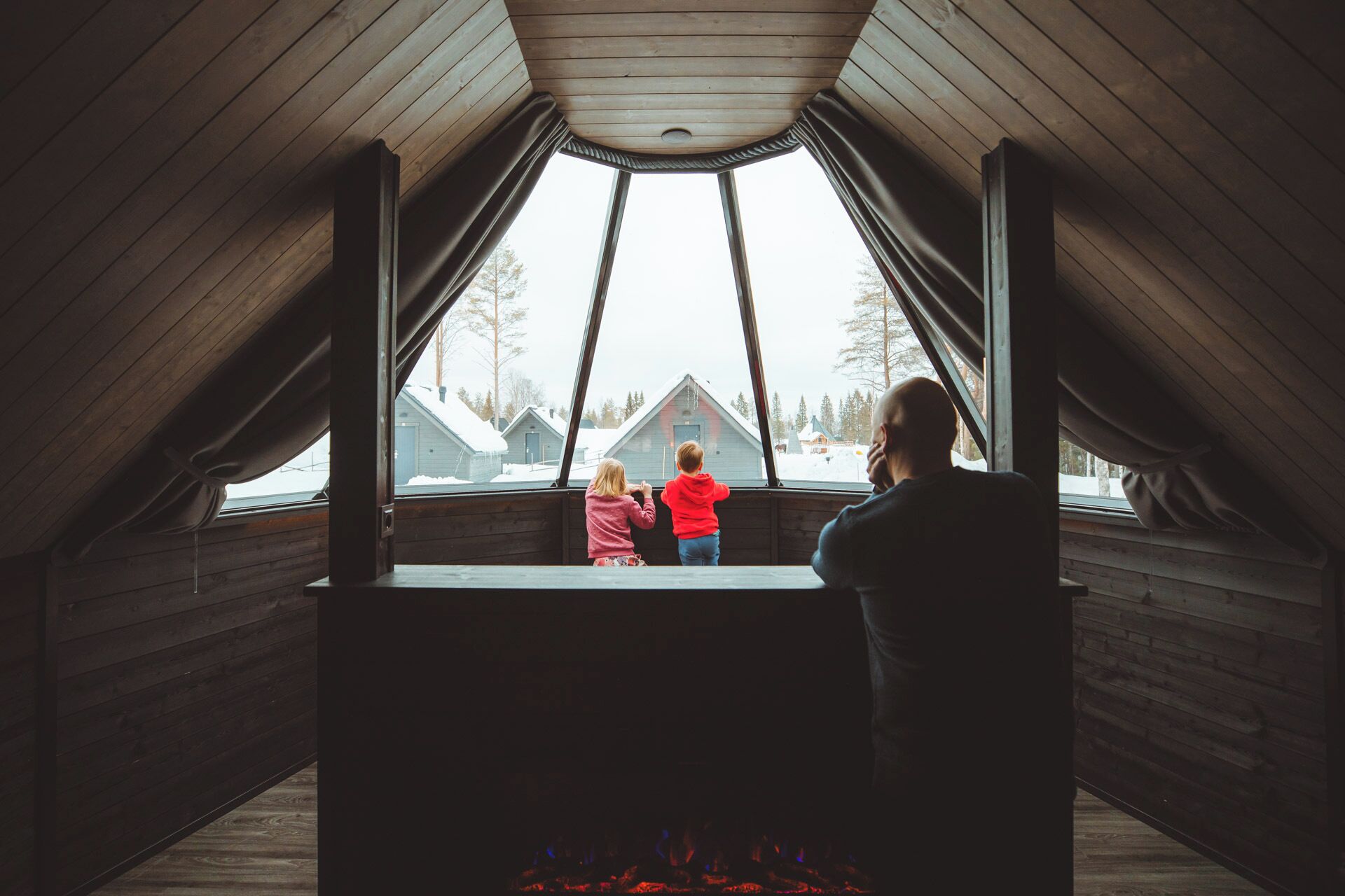 A wooden attic room with a view of snow-covered houses outside.