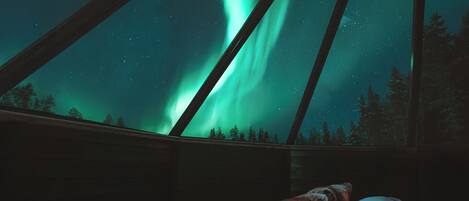 Habitación con vista a las auroras boreales a través de una ventana con vigas de madera.