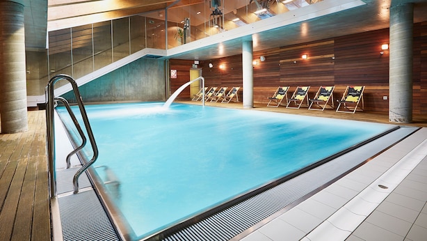 Une piscine intérieure à l’eau claire, dotée d’une échelle en métal et d’un sol carrelé.
