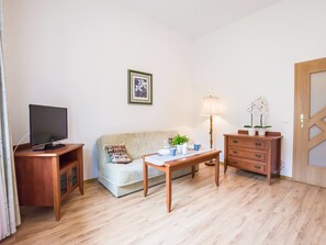 A living room with a television, a sofa, a coffee table, a lamp, and a dresser. - VacationClub - Olymp Apartments (Kolobrzeg)