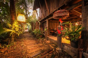 A wooden pathway leading to a rustic building with hanging lamps and potted plants. - Rumah Nyaman Villa (Canggu)