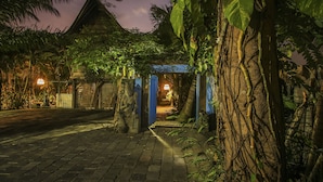 Ein Nachtblick auf ein traditionelles Gebäude mit einem blauen Bogen, umgeben von üppiger Vegetation und einem gepflasterten Weg.