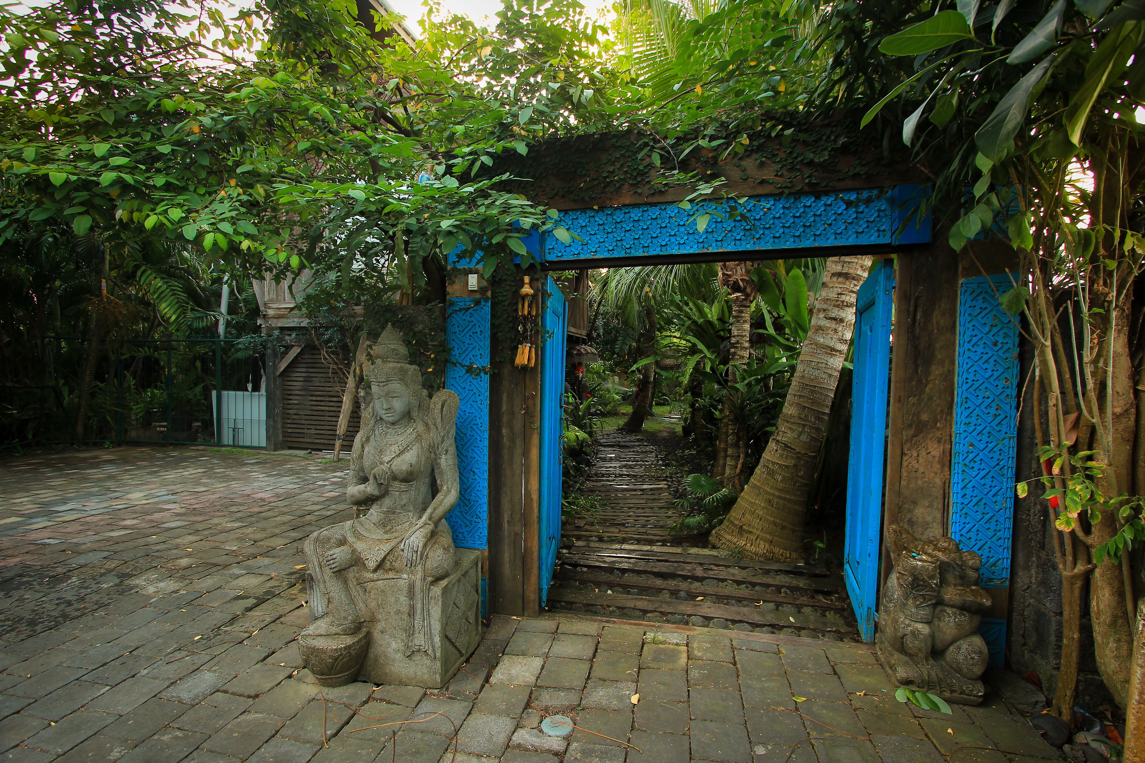 A stone statue of a seated figure, a blue archway, and a staircase leading into a lush garden.