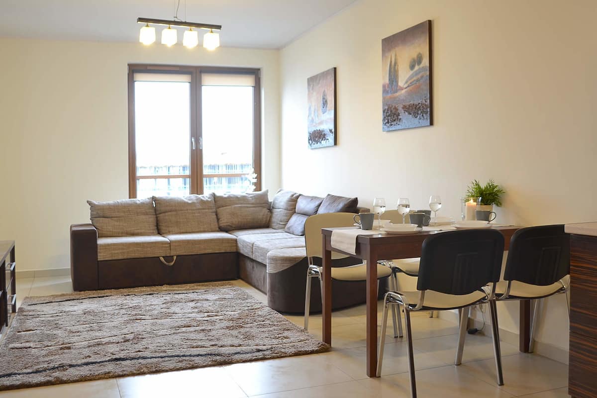Ein modernes Wohnzimmer mit einer Couch, einem Esstisch mit Stühlen, einem Teppich und Kunstwerken an den Wänden.