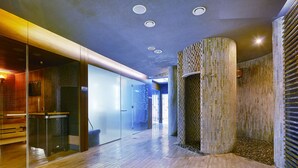 Un couloir moderne avec un plancher en bois, des murs en verre et une colonne centrale ornée de mosaïques.