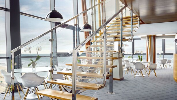 Un intérieur moderne avec un escalier en colimaçon, de grandes fenêtres et une vue sur l’océan.