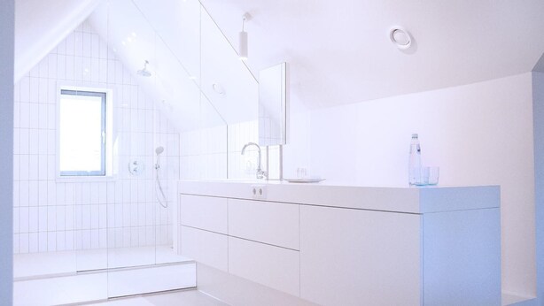 A modern bathroom with a walk-in shower, a large mirror, and a countertop with a sink and a bottle. - Maison Village (Noorbeek)