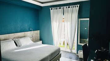 A bedroom with a large bed, a nightstand, a window with white curtains, and a view of the outdoors.