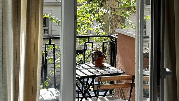 A balcony with a table and chairs, a potted plant, and a view of a tree and buildings. - In Trastevere house (Rome)