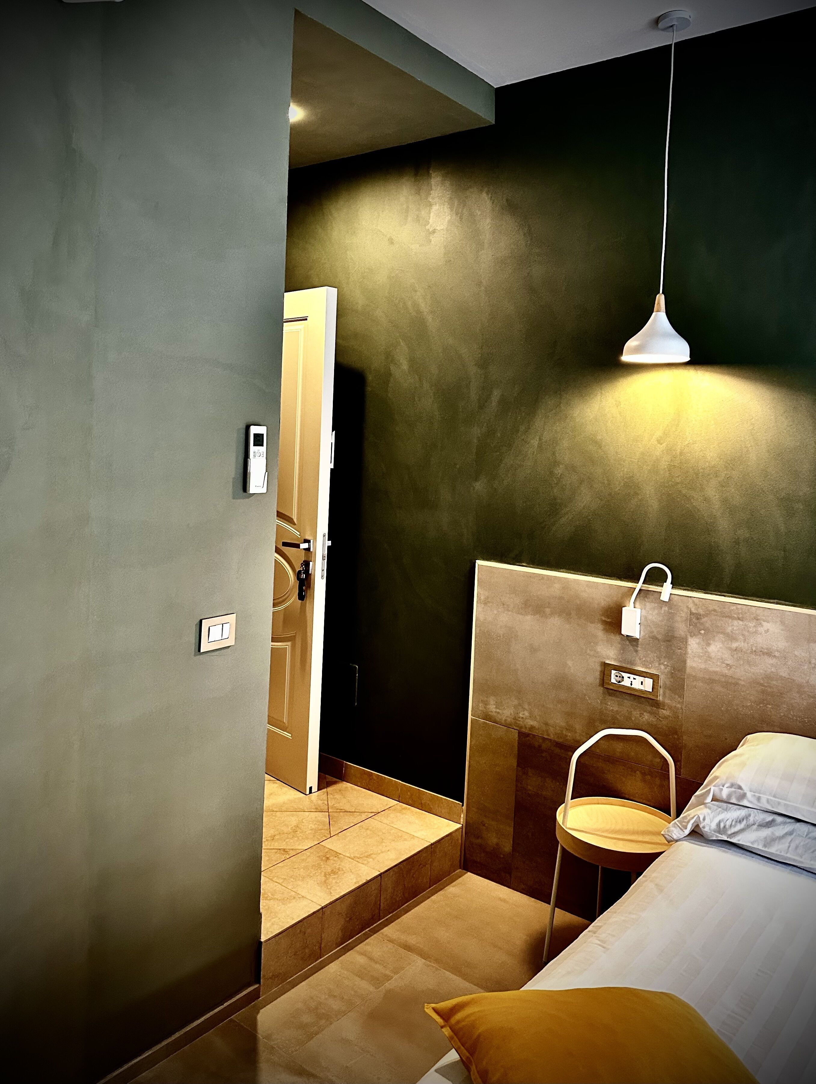 A modern hotel room with a bed, bedside table, and a hanging light fixture.