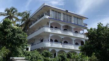 A multi-story building with balconies, parked cars, and a motorcycle in front.