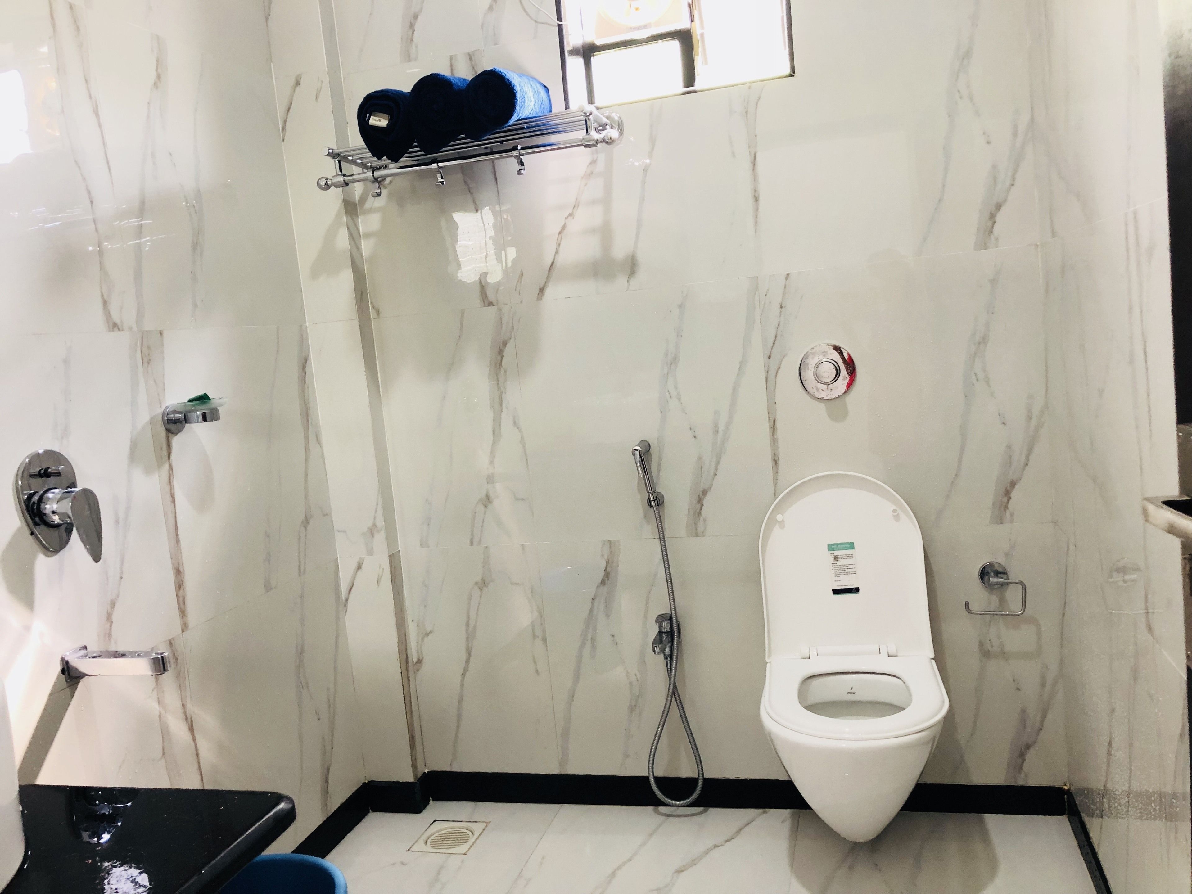 A bathroom with a white toilet, a shower, and a towel rack with rolled towels.