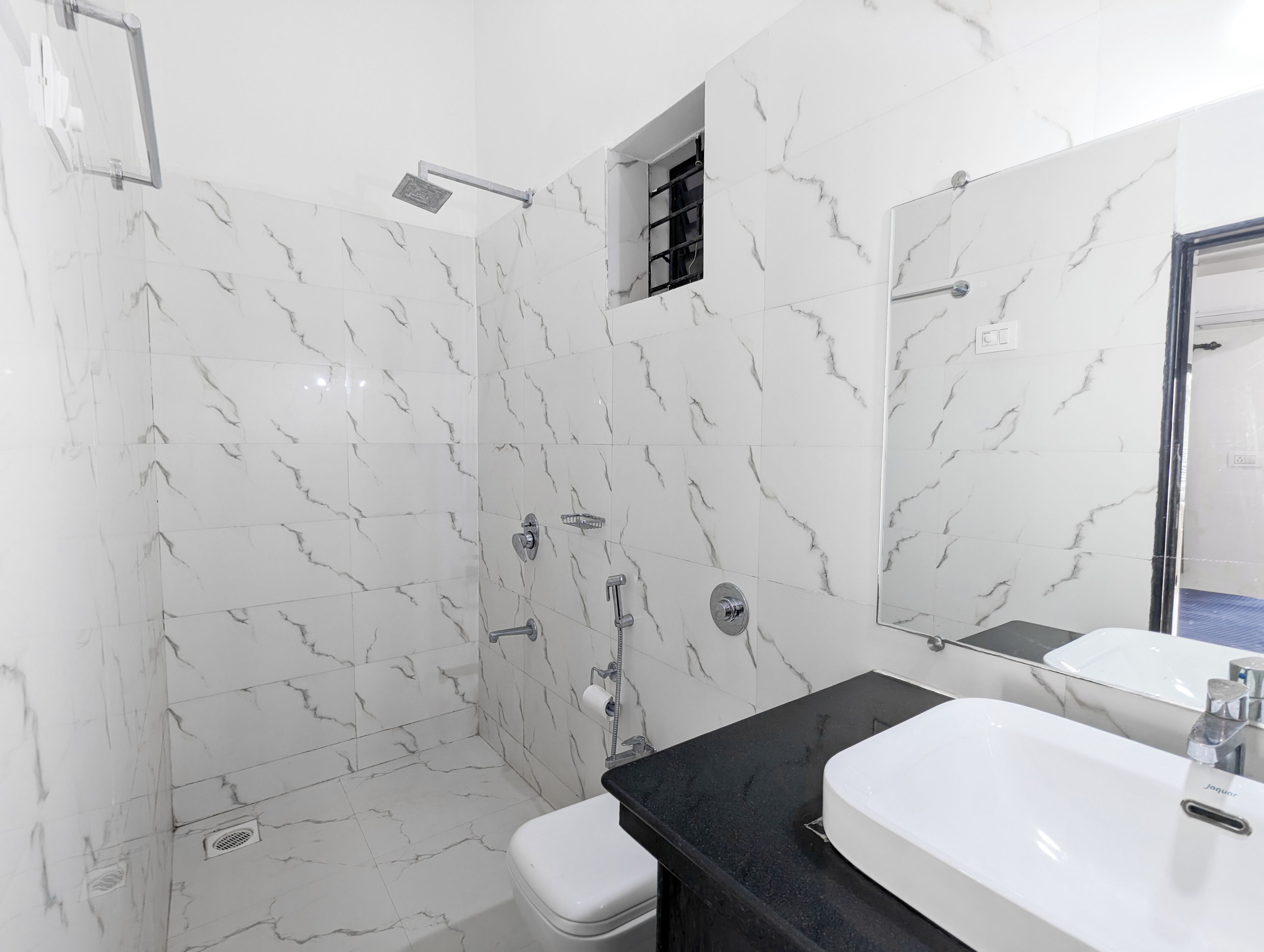 Un baño moderno con paredes de mármol blanco, encimera negra, lavabo blanco y cabina de ducha de vidrio.