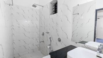 Un baño moderno con paredes de mármol blanco, encimera negra, lavabo blanco y cabina de ducha de vidrio.