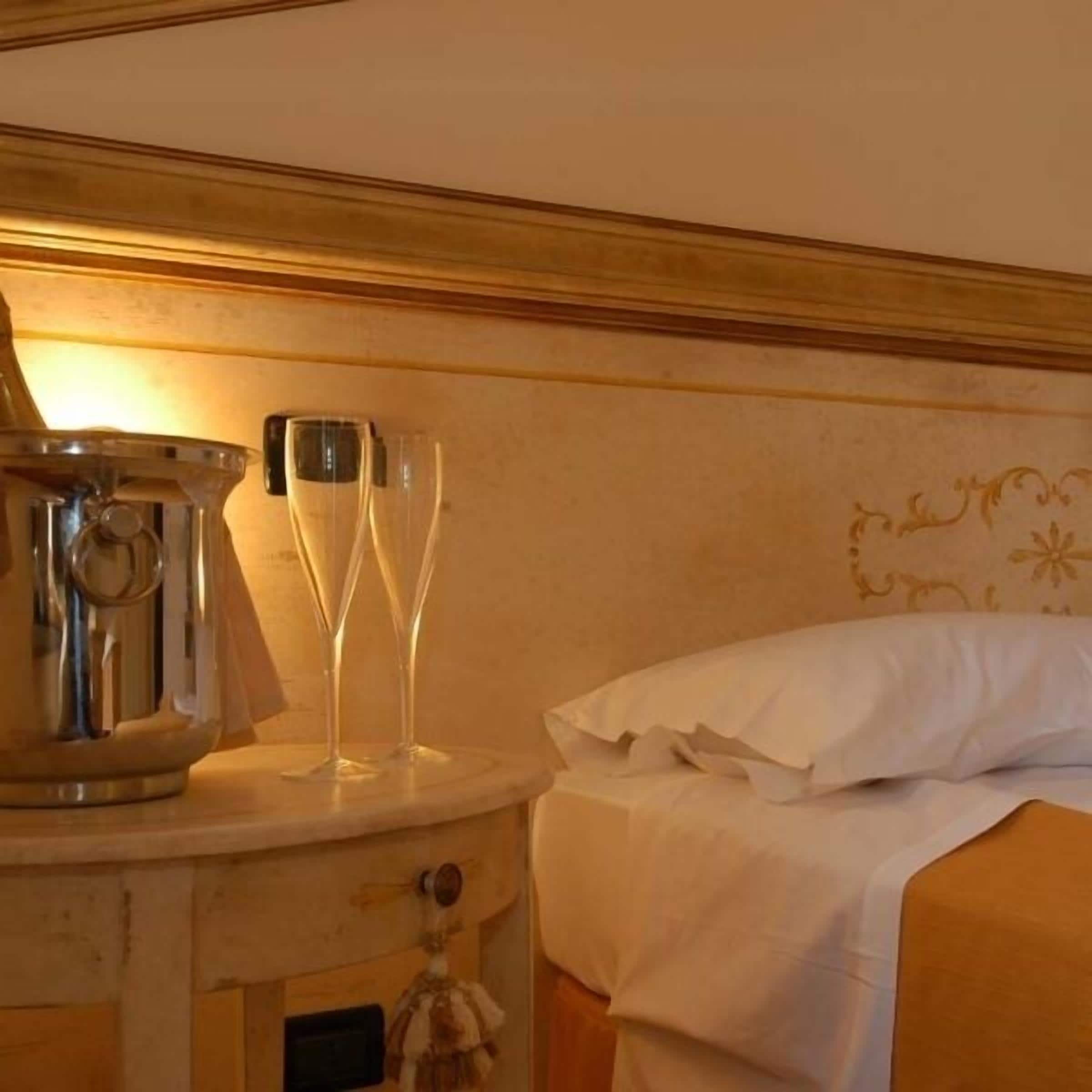 Een hotelkamer met een bed, een nachtkastje met een metalen doos en twee glaasjes.