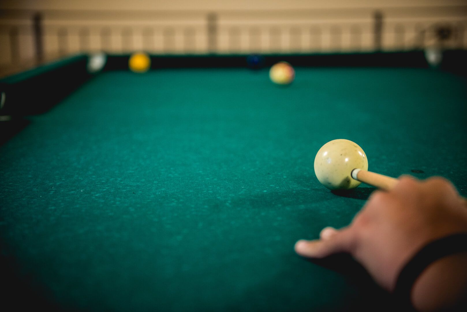 A close-up of a pool table with a cue ball and other balls, a hand holding a pool cue, and a green felt surface.